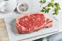 Abatti Ranch American Wagyu New York Strip Diamond 8+ – richly marbled steak on butcher board with herbs