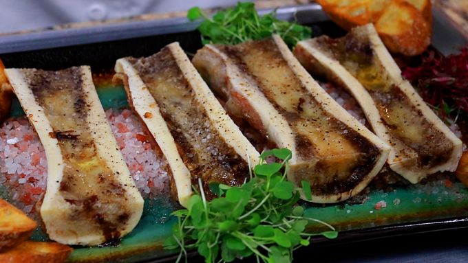 Close-up of cooked marrow scooped onto toasted baguette with sea salt and parsley.